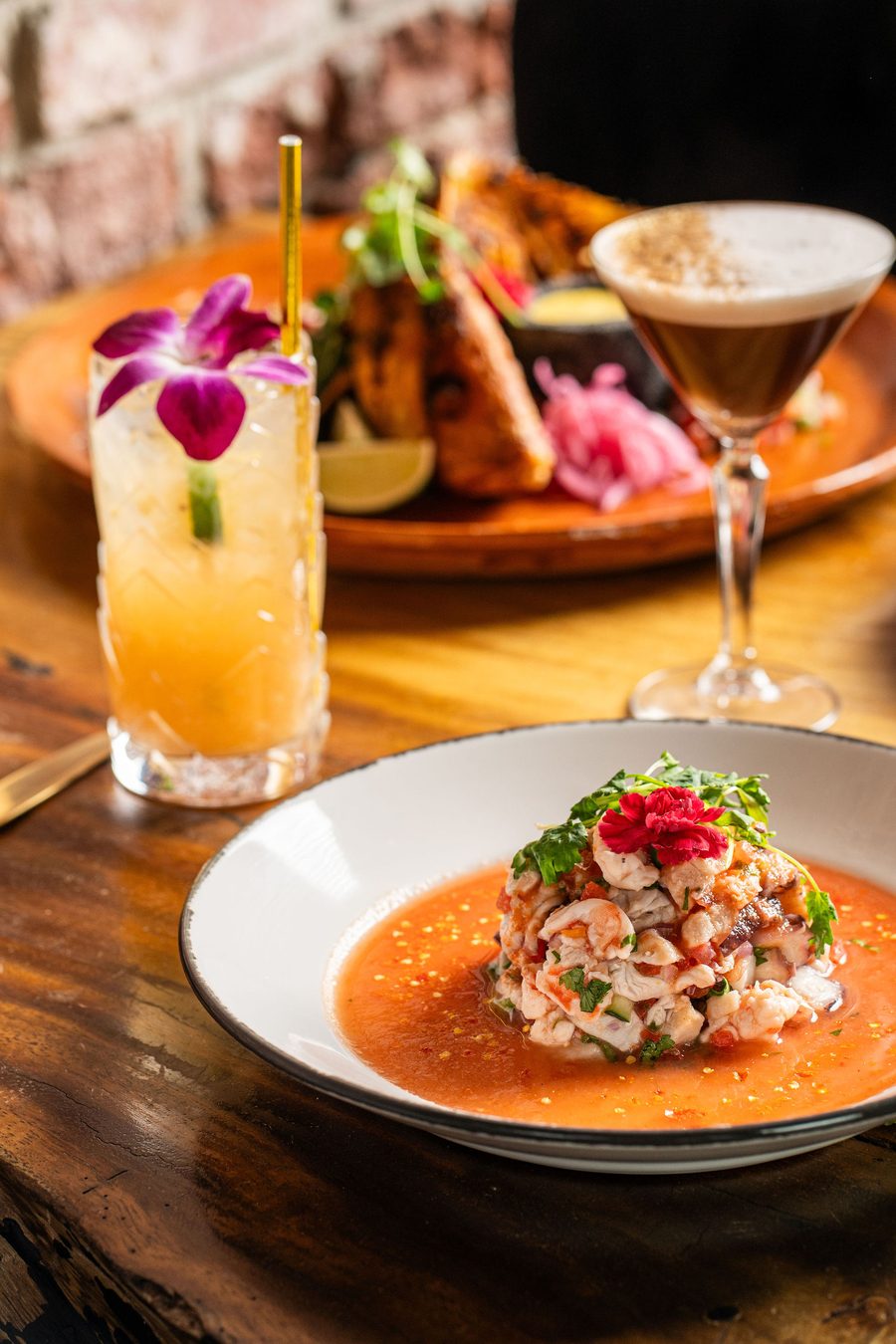 Ceviche with shrimp, octopus and bright tomato broth beside a grapefruit smash cocktail with edible orchid
